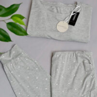 Flat lay shot of Dunnes Stores maternity grey pjs with the top and star print bottoms folded and a green plant hanging over the left side of the image