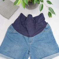 Flat lay image of Kmart over the bump maternity denim shorts with a stripped top and plant in the background
