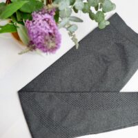 Flat lay image of grey leggings with a small black polka dot motif on the leg with a purple flower in the left corner