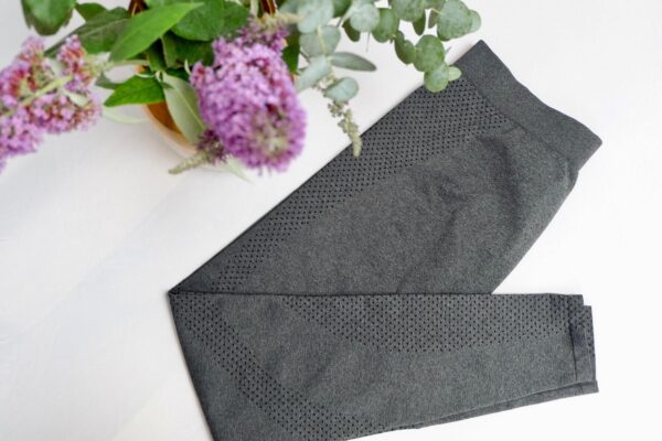 Flat lay image of grey leggings with a small black polka dot motif on the leg with a purple flower in the left corner