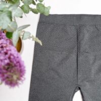 Flat lay image of grey leggings with a small black polka dot motif on the leg with a purple flower in the left corner