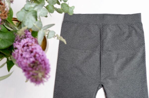 Flat lay image of grey leggings with a small black polka dot motif on the leg with a purple flower in the left corner
