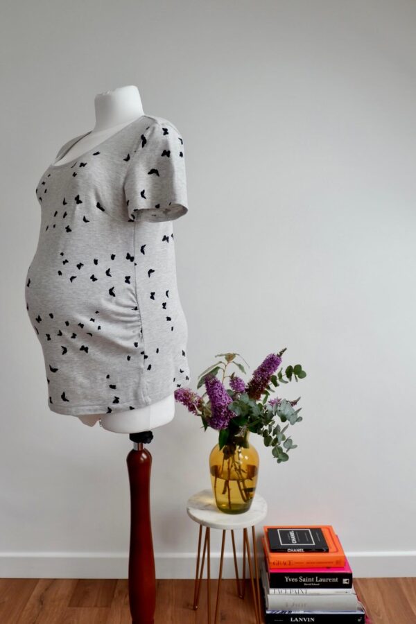 Side view of a maternity light grey t-shirt with a black butterfly print on a pregnant mannequin