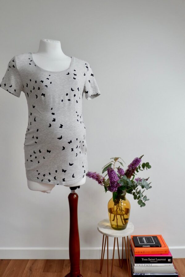 Front view of a maternity light grey t-shirt with a black butterfly print on a pregnant mannequin