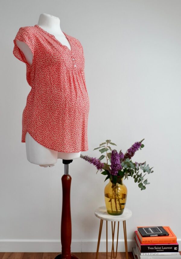 Image of red maternity top with cap sleeves and a daisy print on a mannequin