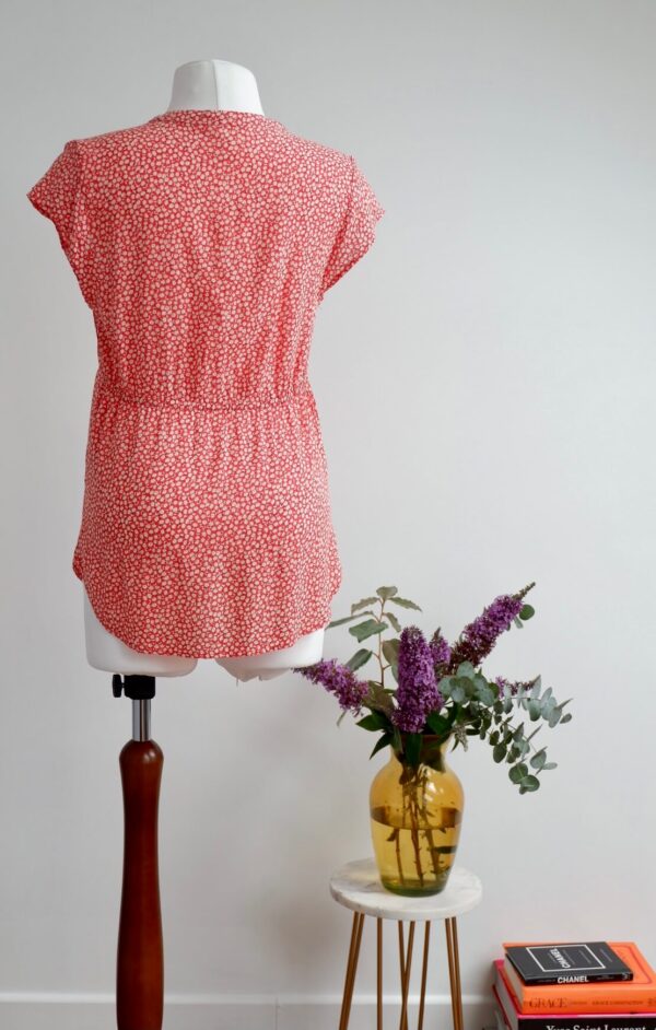 Back image of red maternity top with cap sleeves and a daisy print on a mannequin