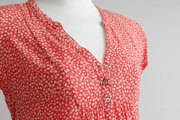 Close up image of the front of a red maternity top with cap sleeves and a daisy print on a mannequin