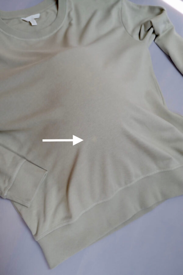 Flat lay image of H&M maternity sage green sweater showing small stain