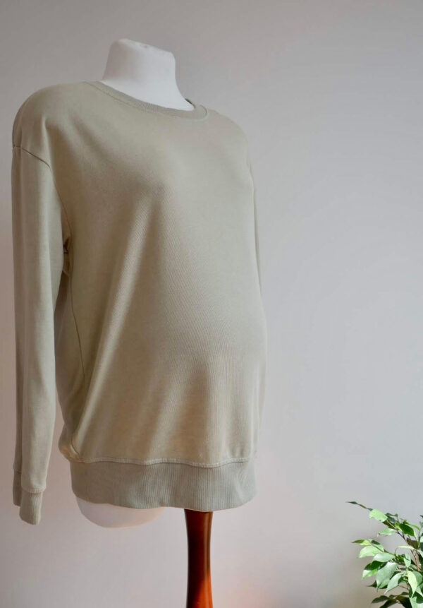 H&M maternity sage green sweater on a mannequin against a white wall