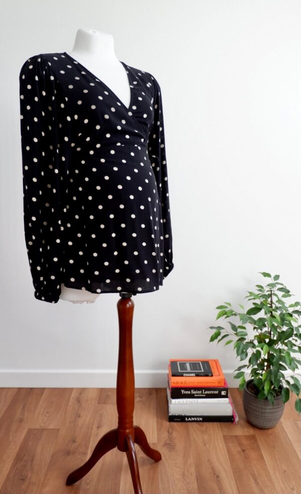 Image of H&M maternity black and cream polka dot maternity wrap top on a mannequin against a white wall.