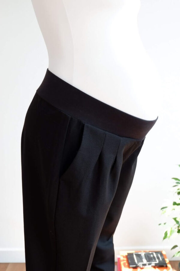 Side view of a pregnant mannequin wearing black trousers showing the mid torso to knees, waistband and pockets of the trousers