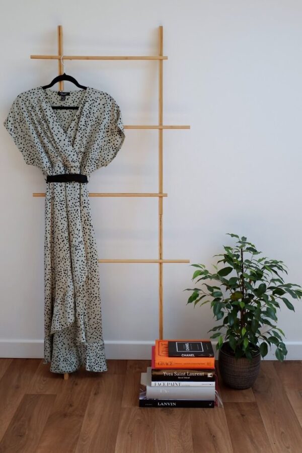 Image of a green satin with small black animal print maternity dress hanging on a ladder against a white wall