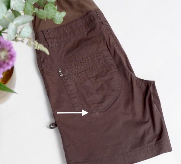 Flat lay image on black maternity shorts folded with an arrow showing a small stain