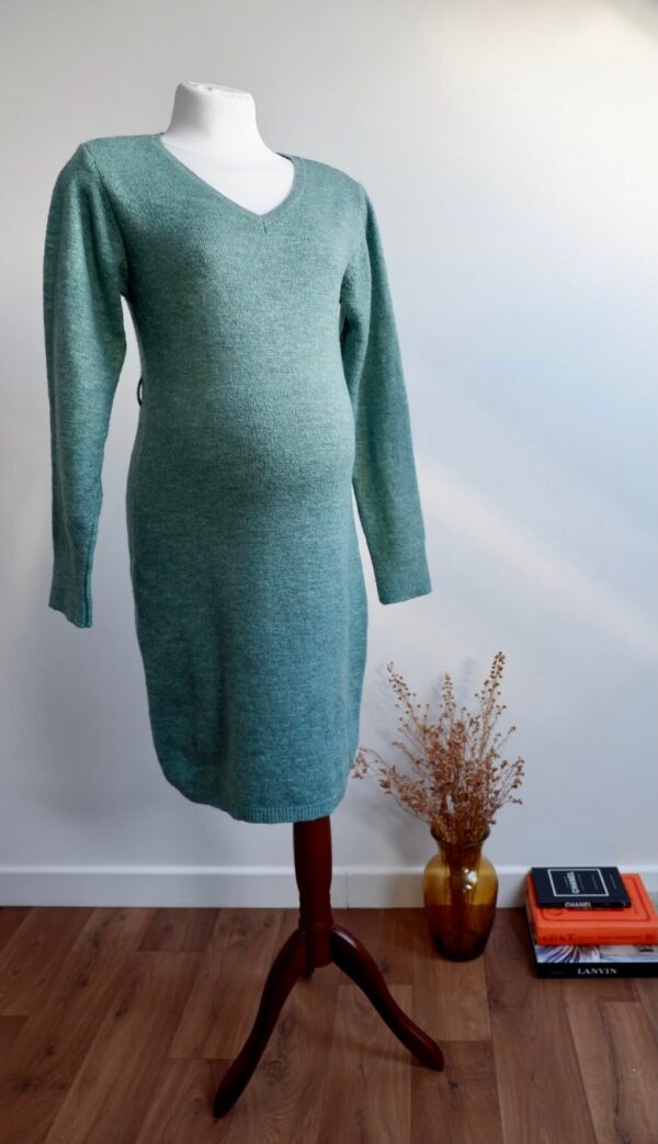 Sage green maternity knit dress on a mannequin agains a white wall