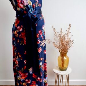 Navy floral maternity maxi dress against a white wall with a vase of dried flowers on a table to the right