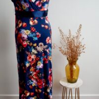 Navy floral maternity maxi dress against a white wall with a vase of dried flowers on a table to the right