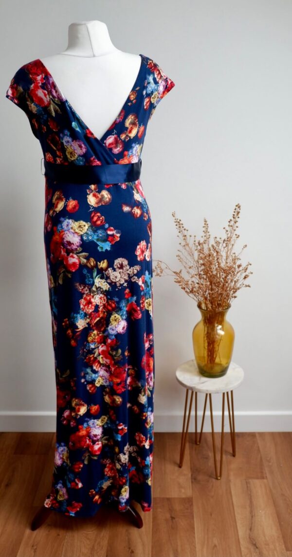 Navy floral maternity maxi dress against a white wall with a vase of dried flowers on a table to the right